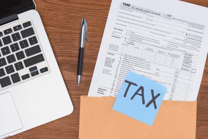 top view of tax form, laptop and blue card with 'tax' word at workplace